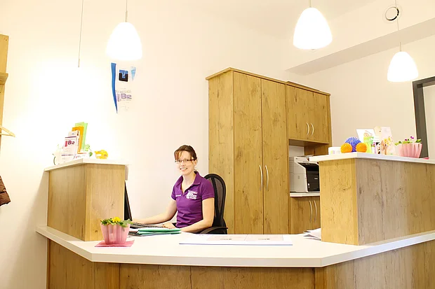 Mitarbeiterin am hellen Empfangstresen aus Holz im Therapiezentrum B12