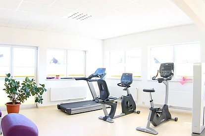 Trainingsbereich mit Laufband, Crosstrainer und Ergometer vor hellen Fenstern