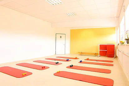 Heller Kursraum mit roten Gymnastikmatten und gelber Wand für Präventionskurse